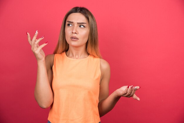 Displeased young woman confused about something on red wall. 