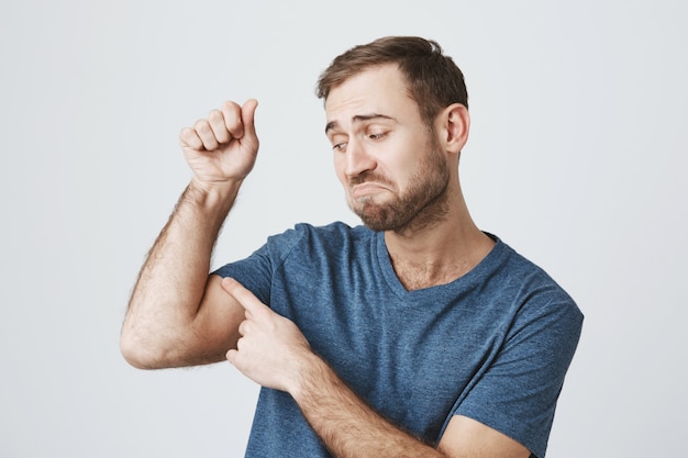 Dissatisfied bearded guy flex weak biceps, lacking strength