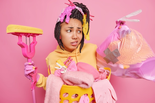 Dissatisfied dark skinned Afro American woman looks unhappily at trash bag