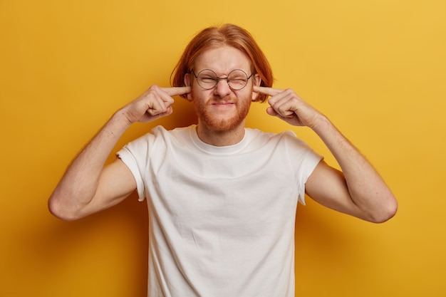 Disturbed ginger man plugs ears, ignores loud music, smirks face