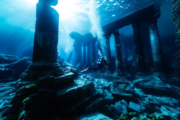 Free photo diver under the sea surrounded by archeological building ruins