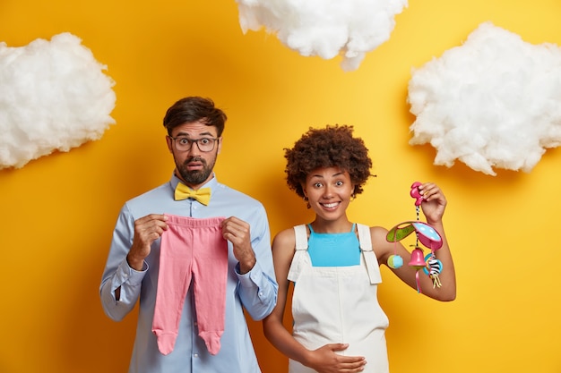 Free Photo diverse couple expect baby pose with toys and clothes for child going to become parents.