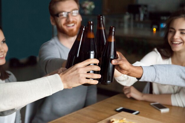 Diverse friends clinking craft beer bottles in pub, cheers concept