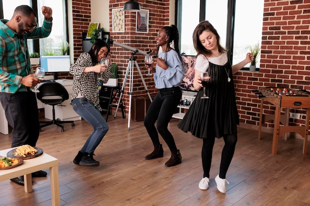 Free photo diverse group of close friends dancing in living room while celebrating birthday event. multicultural people relaxing with music while enjoying wine party at home together.