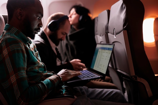 Free photo diverse group of passengers flying in commercial class together to arrive at destination, man using laptop computer during international flight. tourists travelling abroad by airplane.