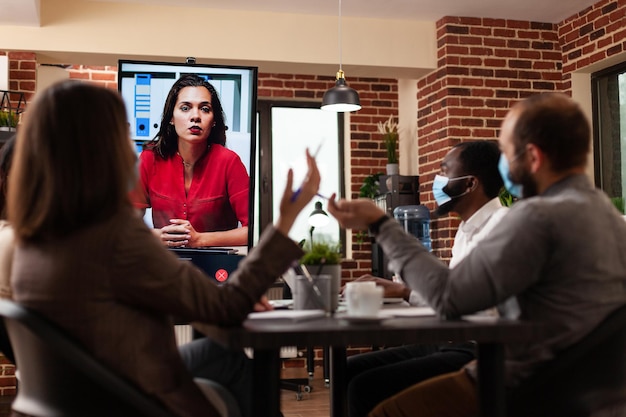 Free photo diverse managers people explaining company strategy to remote woman during online videocall meeting conference working in startup business office. businessteam with medical face mask against covid19