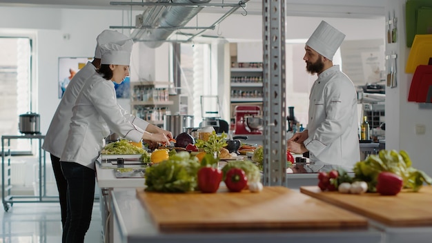 Free photo diverse team of cooks preparing organic ingredients for cuisine dish, making delicious gourmet meal with salad and vegetables in professional kitchen. man and woman cooking food. tripod shot.