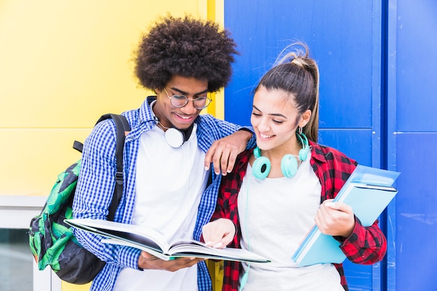 Diverse teenage couple standing against blue and yellow wall studying together