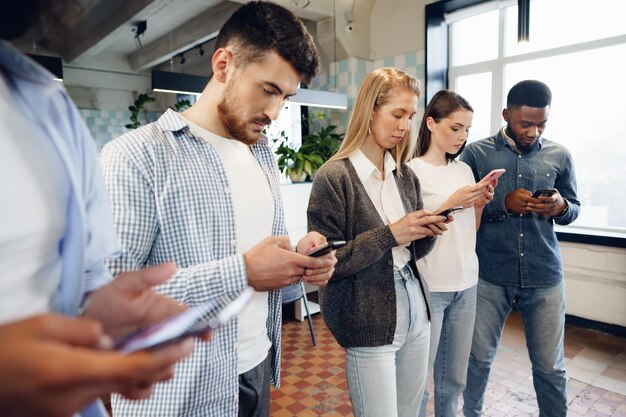 Diverse young people colleagues working on mobile phones together in office