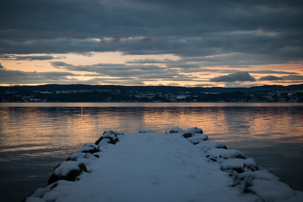 Free Photo dock covered with snow near the sea with the reflection of the sunset