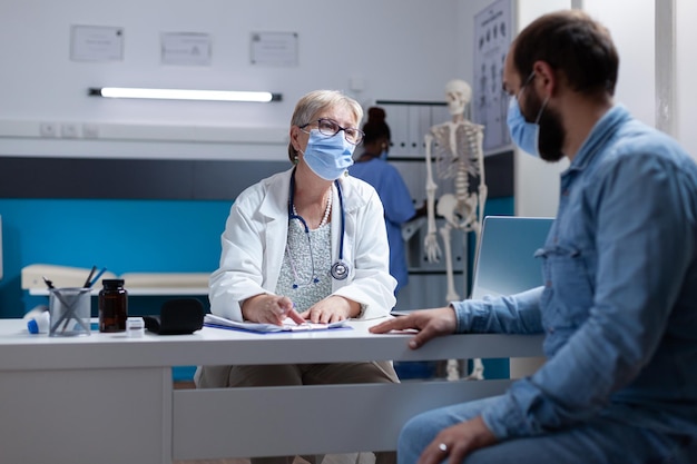 Free photo doctor doing consultation with ill man during covid 19 pandemic in cabinet. woman physician examining patient and helping with healthcare treatment, wearing face mask at checkup visit.