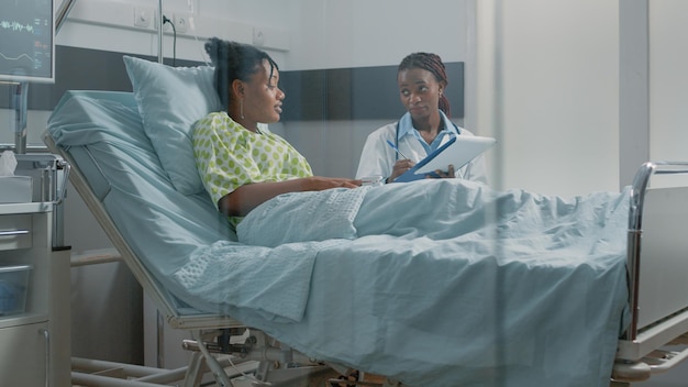 Doctor doing consultation with young patient in hospital ward. General practitioner talking to sick woman to examine illness diagnosis and healthcare treatment for medical recovery.