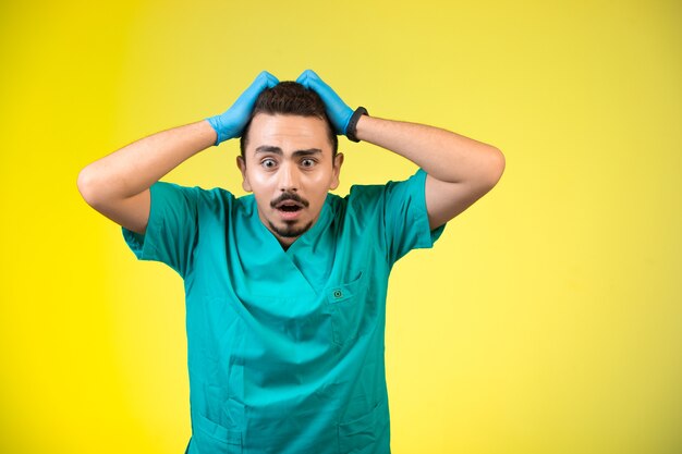 Doctor in green uniform and hand mask frustrated and confused.