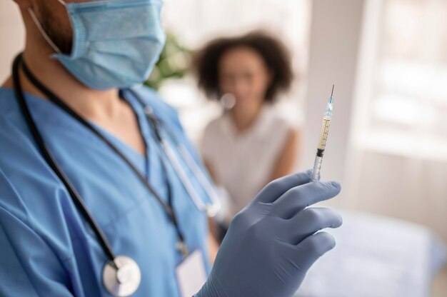 Doctor holding a syringe with vaccine next to a patient