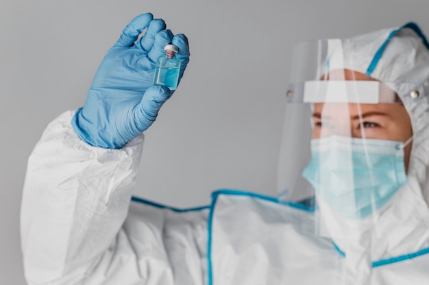 Doctor holding a vaccine bottle while wearing protective equipment