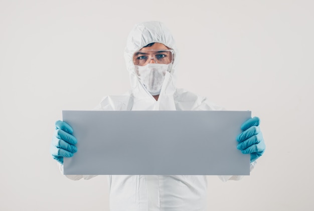 A doctor holding white cardboard in medical gloves and protective suit in light background . space for text coronavirus