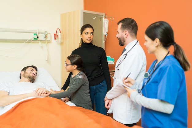 Doctor and nurse explaining disease to woman while standing by sick man at hospital