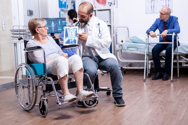 Doctor showing brain X ray image of disabled elderly senior woman in wheelchair