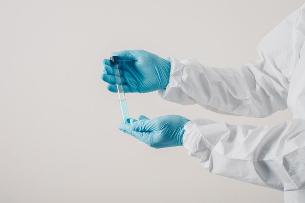 A doctor standing and holding medicine in medical gloves and protective suit in light background .  