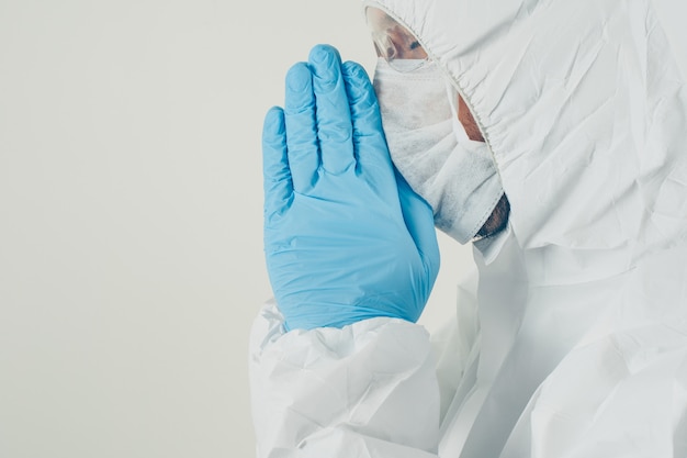 Free Photo a doctor standing and praying in mask, gloves and protective suit