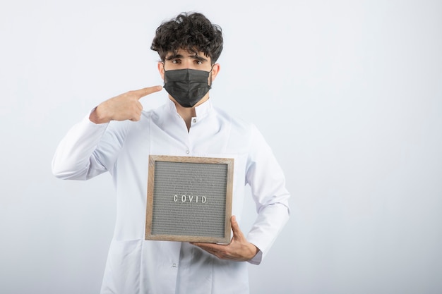 Free photo doctor in white coat with stethoscope pointing at mask isolated on white.