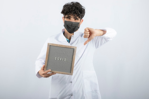 Free photo doctor in white coat with stethoscope showing a thumb down isolated on white.