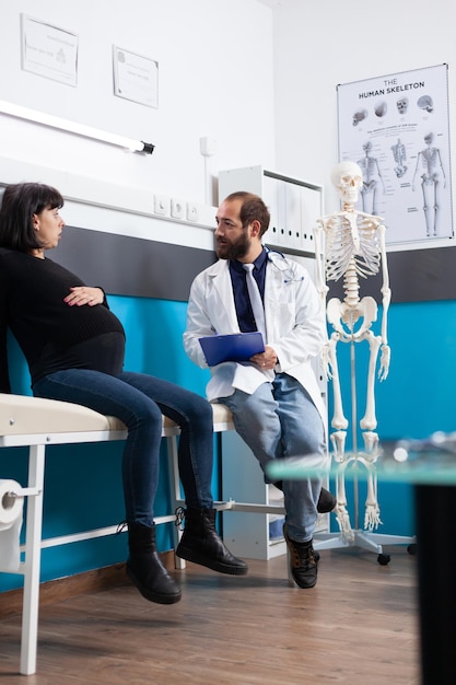 Free photo doctor with clipboard consulting pregnant woman at exam appointment in office. expectant patient discussing about childbirth and pregnancy with physician, receiving support at checkup visit.