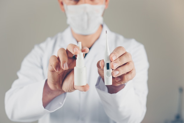 Free photo a doctor with mask holding thermometer and nasal spray in his hands. side view.