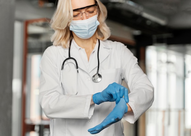 Doctor with medical mask putting on medical gloves