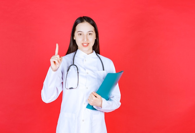 Doctor with a stethoscope holding the history of the patient and raising hand to ask a question.