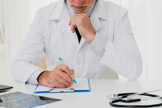 Free Photo doctor writing on clipboard with hand on chin