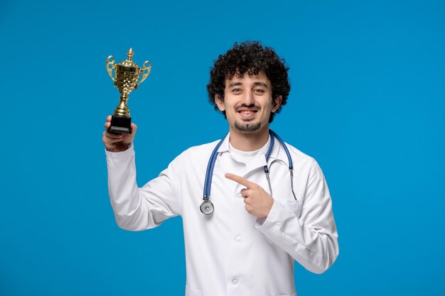 Doctors day curly handsome cute guy in medical uniform smiling and holding a trophy