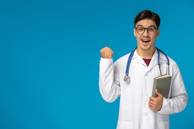 Doctors day handsome brunette cute guy in medical gown happy holding a book