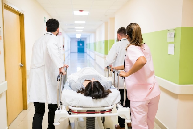 Doctors and nurse pushing female patient on stretcher at corridor in hospital