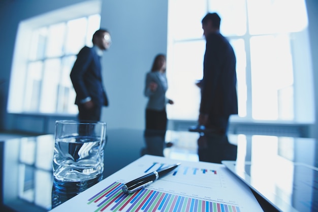 Documents with charts and a glass of water on the desk