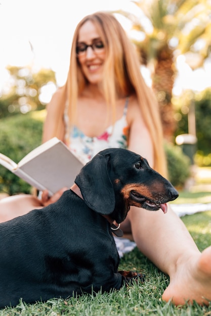 Free Photo dog sitting in front of smiling young woman reading book