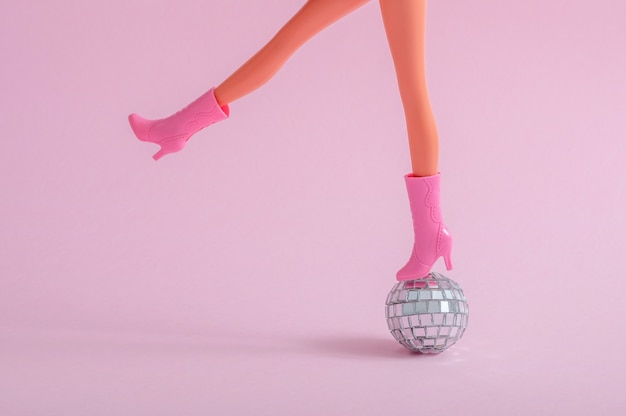 Free photo doll feet on a small disco ball on a pink wall