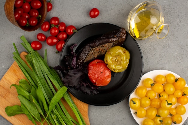 Dolma famous meat meal from east inside black plate along with fresh ripe yellow and red tomatoes and olive oil