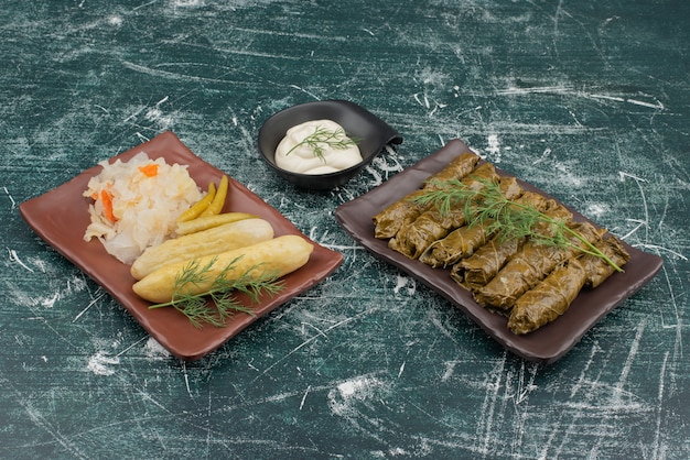 Dolma with sour cream and plate of salt cabbage and cucumber .