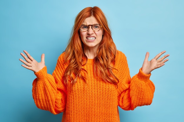 Free photo dont tell me about this nonsense. annoyed young redhead woman clenches teeth frowns face and raises palms angrily expresses irritation wears knitted sweater.