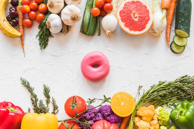 Donut between the colorful healthy and unhealthy food on white textured background