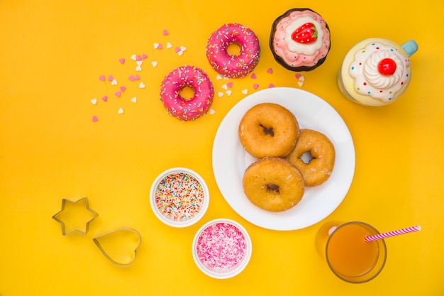 Donuts, juice, cupcakes and pastry cutter on yellow background