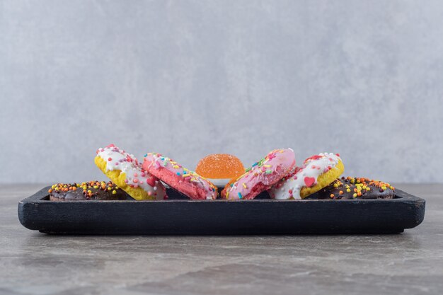 Donuts and a marmelade bundled on a black tray on marble surface