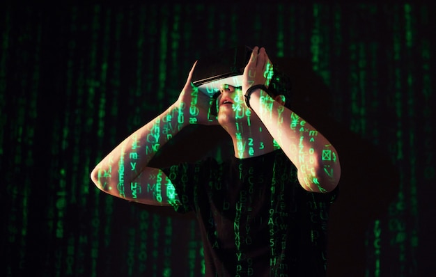 Double exposure of a caucasian man and Virtual reality VR headset is presumably a gamer or a hacker cracking the code into a secure network or server, with lines of code in green