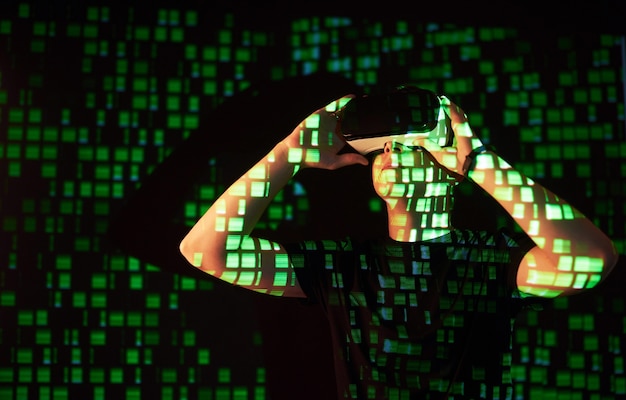 Double exposure of a caucasian man and Virtual reality VR headset is presumably a gamer or a hacker cracking the code into a secure network or server, with lines of code in green