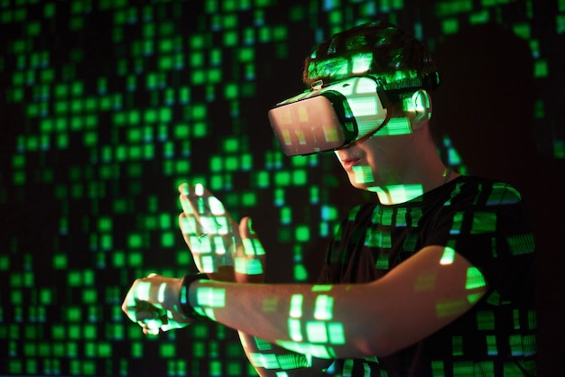 Double exposure of a caucasian man and Virtual reality VR headset is presumably a gamer or a hacker cracking the code into a secure network or server, with lines of code in green