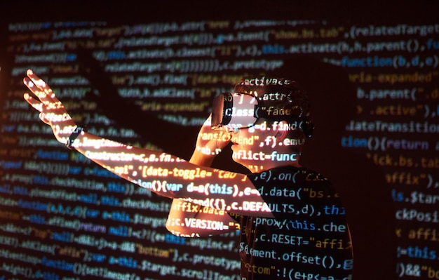 Double exposure of a caucasian man and Virtual reality VR headset is presumably a gamer or a hacker cracking the code into a secure network or server, with lines of code