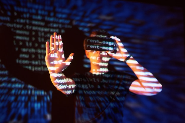 Double exposure of a caucasian man and Virtual reality VR headset is presumably a gamer or a hacker cracking the code into a secure network or server, with lines of code