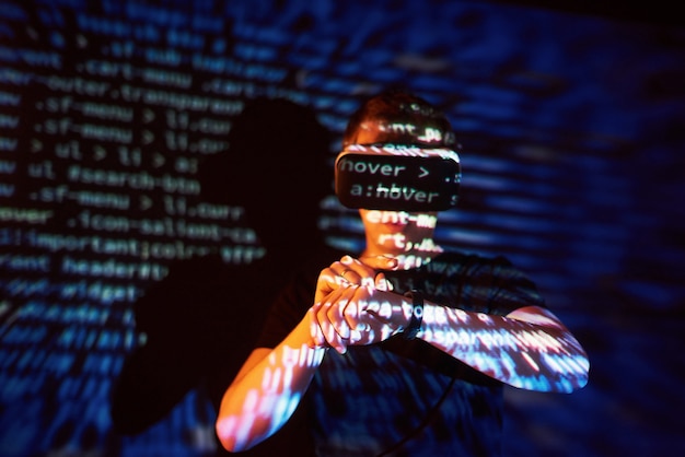 Double exposure of a caucasian man and Virtual reality VR headset is presumably a gamer or a hacker cracking the code into a secure network or server, with lines of code