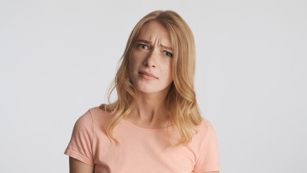 Doubtful blond girl thoughtfully looking in camera isolated on white background. What expression